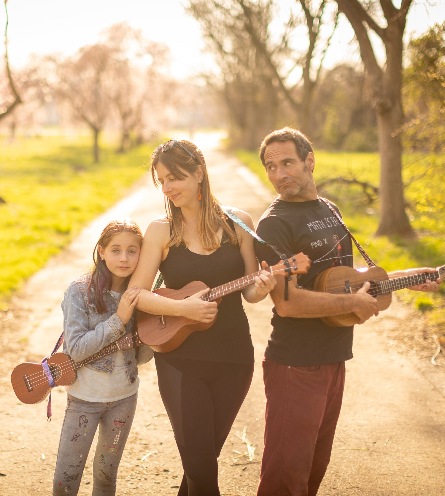 Family of three stand outside in the spring holding ukuleles